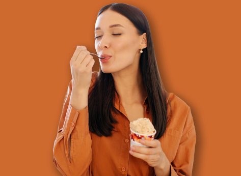 Happy young woman enjoy eating tasty ice cream with closed eyes, sitting in kitchen interior at home, free space