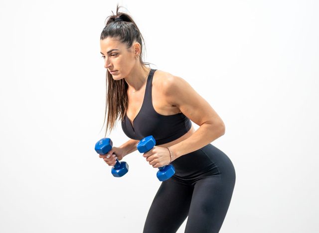Fit woman doing bent-over rows with dumbbells in minimal indoor studio gym setup