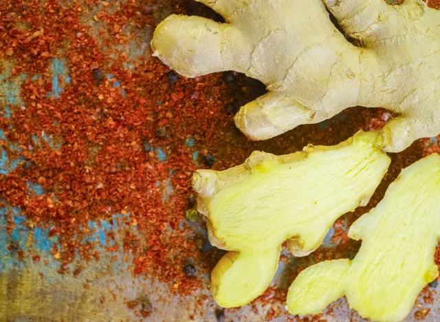 Fresh organic ginger root with powdered Cayenne pepper on the wooden table, used as food ingredient and for medicine.