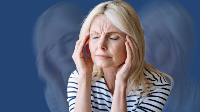 Portrait of mature woman touching, massaging temples and suffering from severe head ache. Problems with memory, disorder. Female sitting on armchair at home
