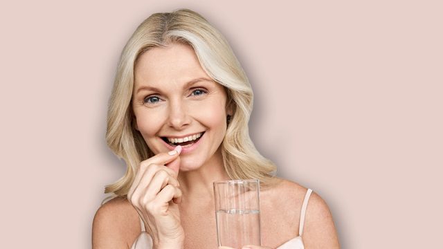 Happy middle aged 50s woman holding pill and glass of water taking dietary supplements. Portrait of smiling adult attractive woman taking care of health in menopause, isolated on white.