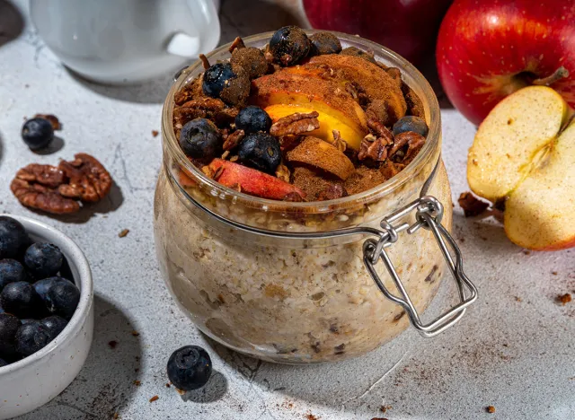 Healthy vegan dietary breakfast or snack. Apple pie overnight oatmeal, oats flakes with apples, yogurt, cinnamon, spices, blueberry. In glass, on a white marble table. Copy space