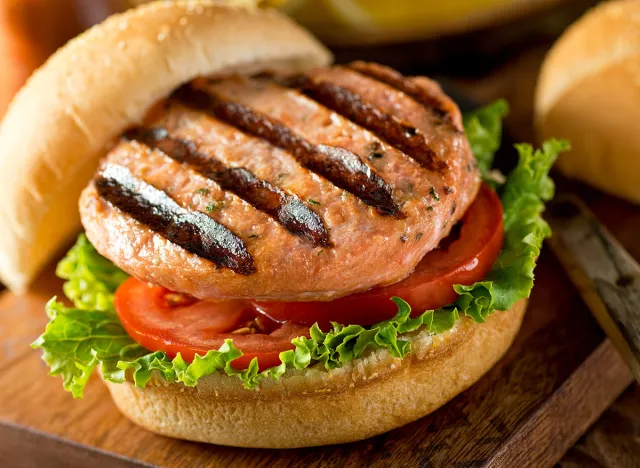A delicious homemade grilled salmon burger with tomato and lettuce on a bun.