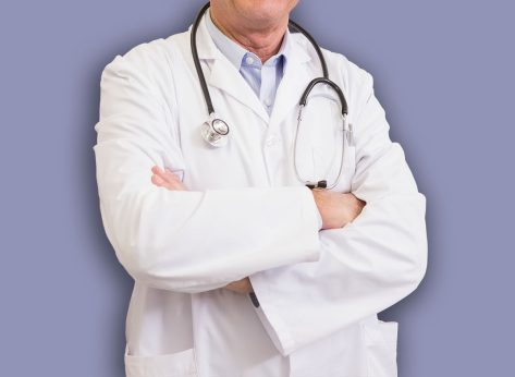Doctor with arms crossed with colleague behind him in the pharmacy