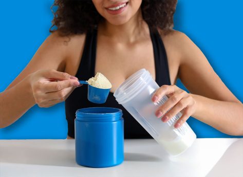 Beautiful woman making protein shake at white table indoors, closeup