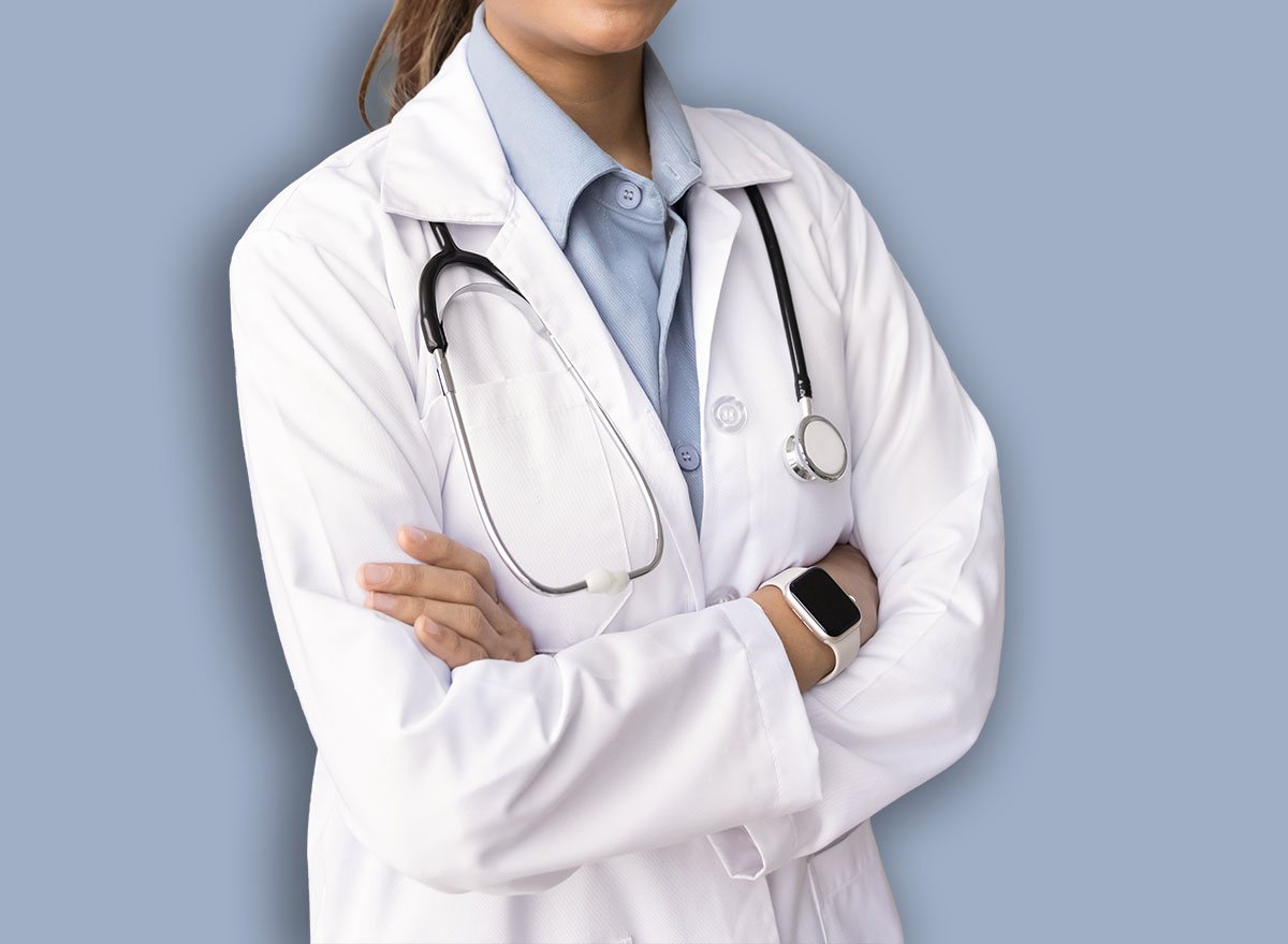 Positive young Indian medical specialist woman posing for portrait in ultrasound diagnosing examination room, standing with hands crossed, looking at camera. Confident doctor woman portrait