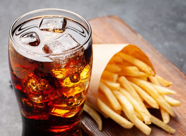 Glass of cola with ice cubes and potato fries chips. Fast food take away