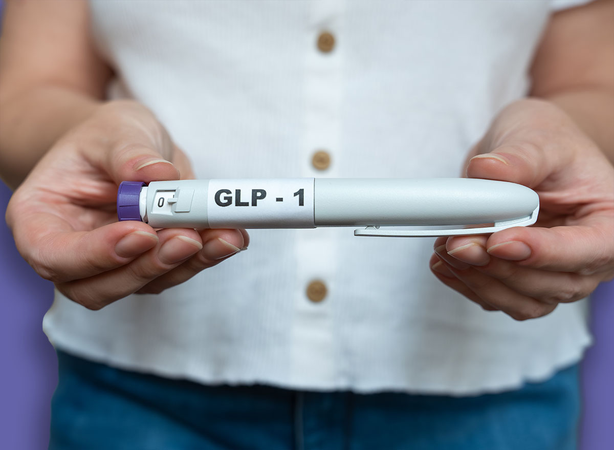 Close-up of a woman holding a GLP-1 injection pen in both hands with her bare abdomen visible in the background. The image illustrates weight management, hormone therapy, modern medical treatment, and