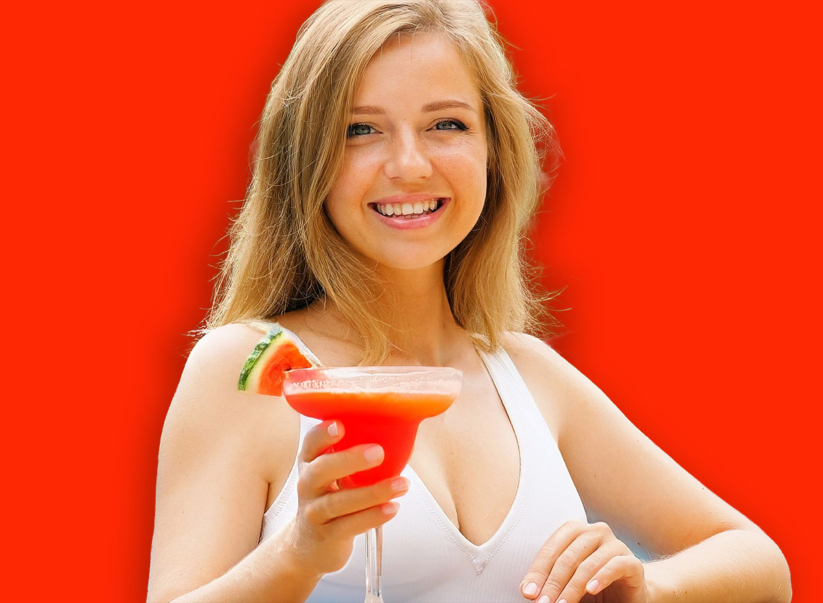 Beautiful woman in white swimsuit relaxing, enjoying cocktail by outdoor pool. Happy, smiling and having fun. Travel, vacation, tropical holidays.