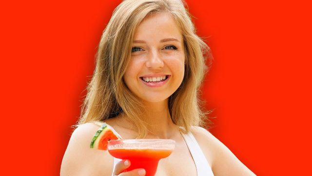 Beautiful woman in white swimsuit relaxing, enjoying cocktail by outdoor pool. Happy, smiling and having fun. Travel, vacation, tropical holidays.