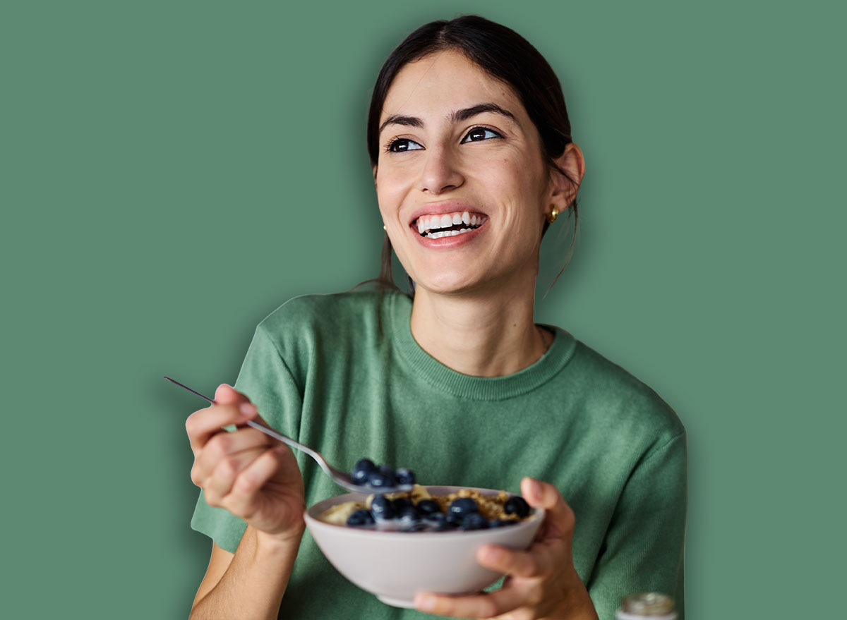 Portrait of a young woman preparing and eating breakfast, drinking juice in the kitchen at home