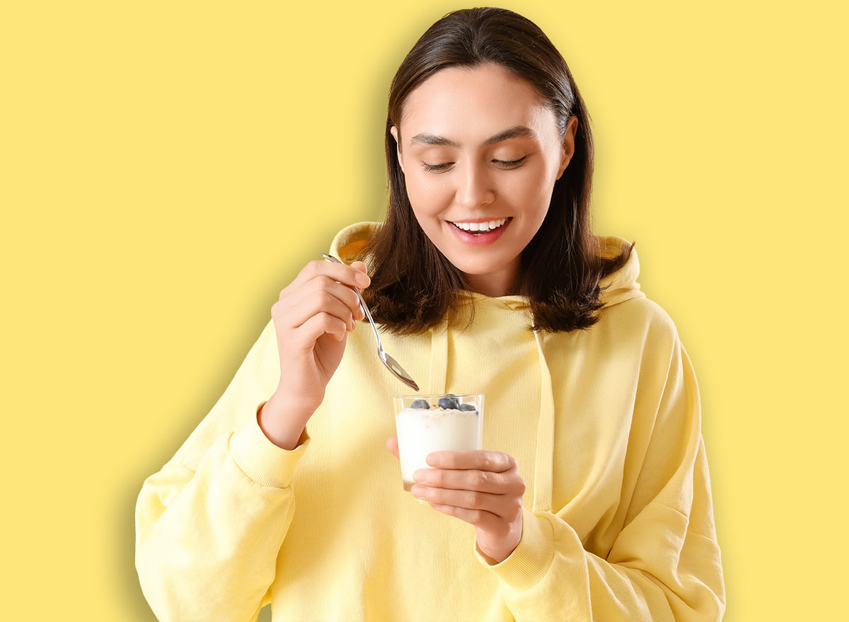 Happy young woman with glass of tasty yoghurt on yellow background