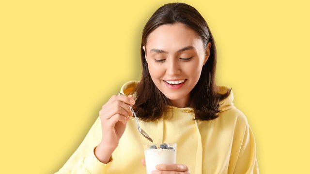 Happy young woman with glass of tasty yoghurt on yellow background