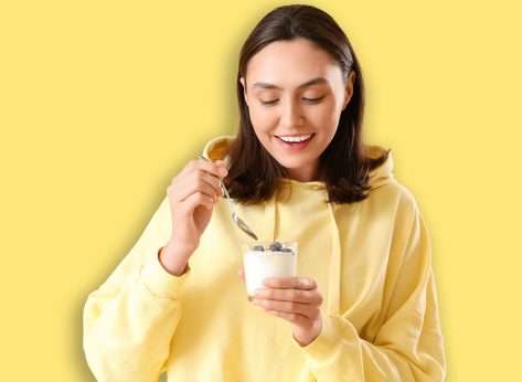 Happy young woman with glass of tasty yoghurt on yellow background
