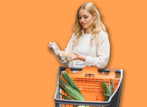 Young adult woman pushing shopping trolley between the shelves in the market.